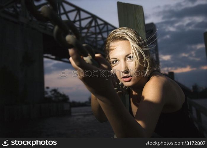 Caucasian mid-adult blonde woman clinging to chain rail beside bridge.