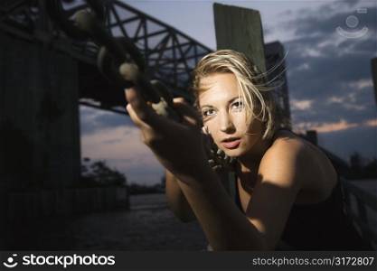 Caucasian mid-adult blonde woman clinging to chain rail beside bridge.
