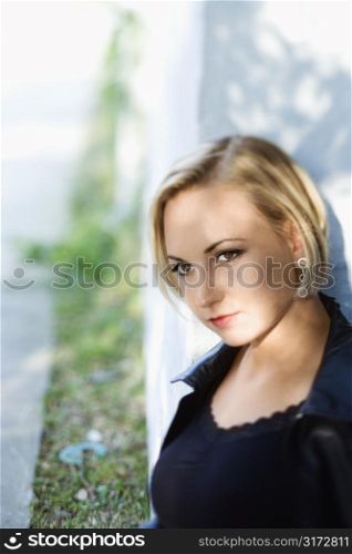 Caucasian mid-adult blonde woman standing against sun dappled building.