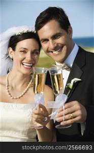 Caucasian mid-adult bride and groom toasting champagne looking at viewer and smiling.