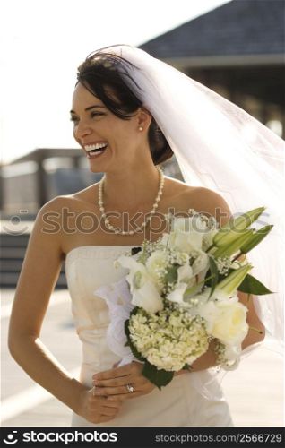 Caucasian mid-adult bride holding flower bouquet and smiling.