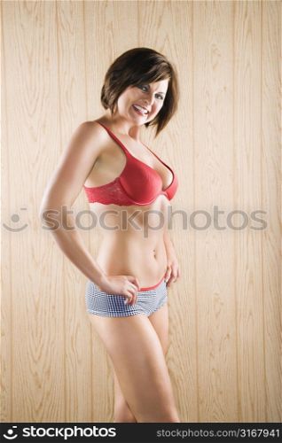 Caucasian mid adult brunette woman in lingerie smiling at viewer with hands on hips.