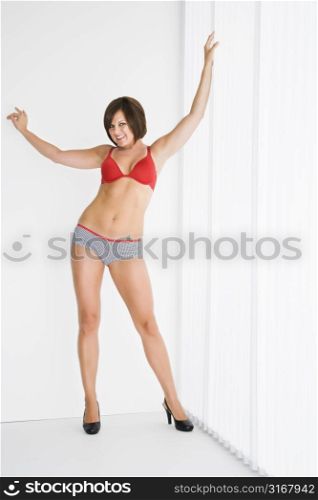 Caucasian mid adult brunette woman in lingerie with arms raised smiling at viewer.
