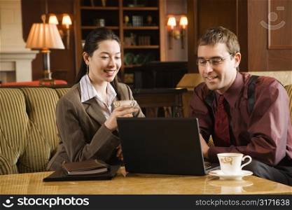 Caucasian mid adult businessman and woman drinking coffee and looking at laptop computer.