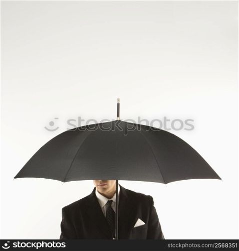 Caucasian mid-adult businessman holding umbrella with face covered.