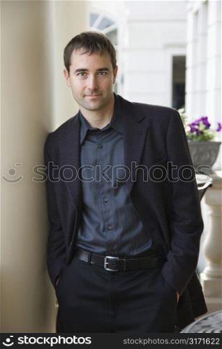 Caucasian mid adult businessman leaning with hands in pockets smiling at viewer.