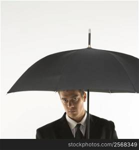 Caucasian mid-adult businessman looking out at viewer from under umbrella.