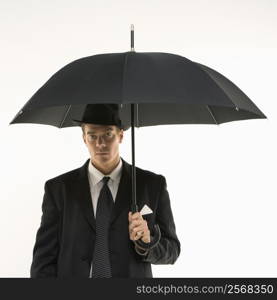 Caucasian mid-adult businessman wearing fedora holding umbrella and looking at viewer.