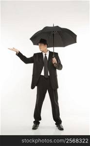 Caucasian mid-adult businessman wearing fedora holding umbrella with arm outstretched.