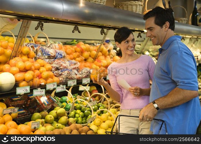 Caucasian mid-adult couple grocery shopping for fruit looking at each other smiling.