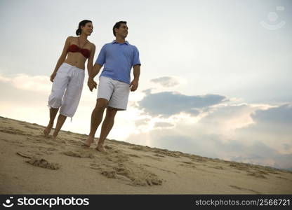 Caucasian mid-adult couple holding hands walking on beach.