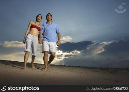 Caucasian mid-adult couple holding hands walking on beach.