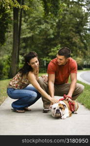 Caucasian mid adult couple petting English Bulldog on sidewalk.