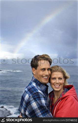 Caucasian mid-adult couple standing by ocean with rainbow in background in Maui, Hawaii.