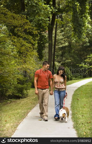 Caucasian mid adult couple walking English Bulldog in park.