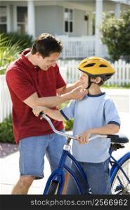 Caucasian mid-adult dad strapping bicycle helmet on pre-teen son.