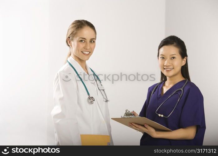 Caucasian mid-adult female doctor and Asian Chinese mid-adult female physician&acute;s assistant standing together smiling and looking at viewer.