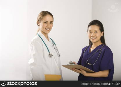 Caucasian mid-adult female doctor and Asian Chinese mid-adult female physician&acute;s assistant standing together smiling and looking at viewer.