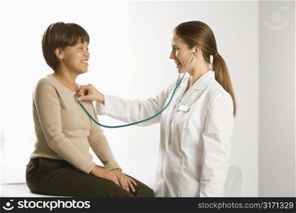 Caucasian mid-adult female doctor examining African American middle-aged female patient with stethoscope.