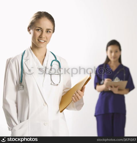 Caucasian mid-adult female doctor smiling and looking at viewer with Asian Chinese mid-adult female physician&acute;s assistant standing in background.