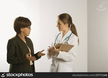 Caucasian mid-adult female doctor talking with African American middle-aged female patient.