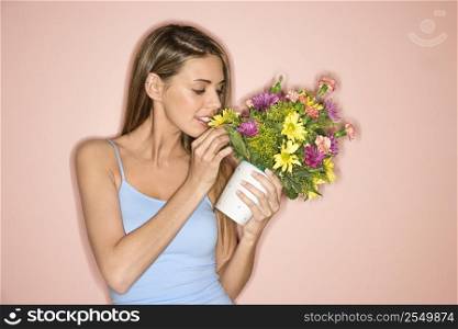 Caucasian mid-adult female holding pot of flowers and smelling them.