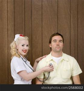Caucasian mid-adult female nurse checking male&acute;s heartbeat by wood paneling.