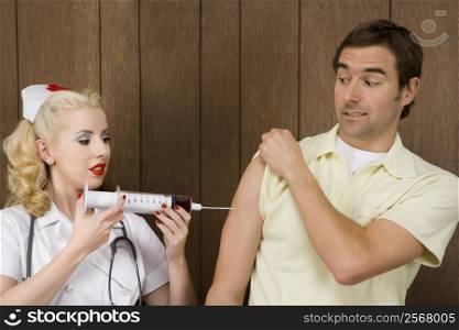 Caucasian mid-adult female nurse giving shot to man with oversized syringe.