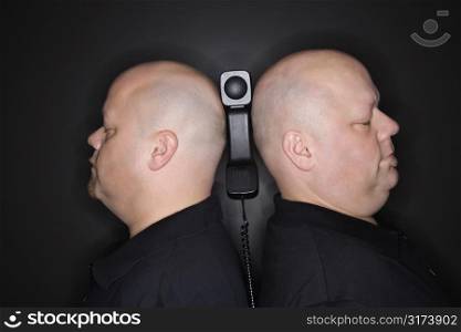 Caucasian mid adult identical twin men standing back to back with telephone balancing between them.