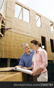 Caucasian mid-adult male and female looking at blueprints in construction phase of house.