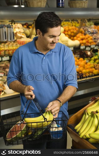 Caucasian mid-adult male grocery shopping for bananas.