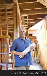Caucasian mid-adult male holding blueprints in building construction site.