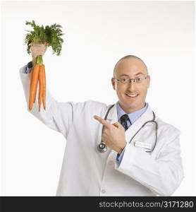 Caucasian mid adult male physician holding and pointing to bunch of carrots.