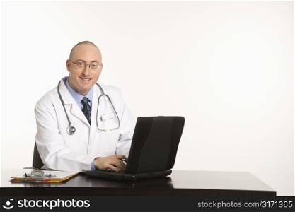 Caucasian mid adult male physician sitting at desk with laptop computer.