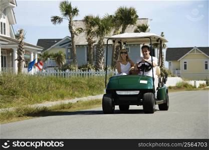 Caucasian mid-adult man and woman driving golf cart down residential street.
