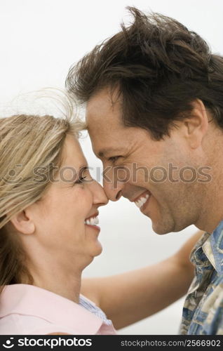 Caucasian mid-adult man and woman holding each other and looking into each other&acute;s eyes on beach.