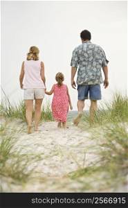 Caucasian mid-adult man and woman walking with female child toward beach.