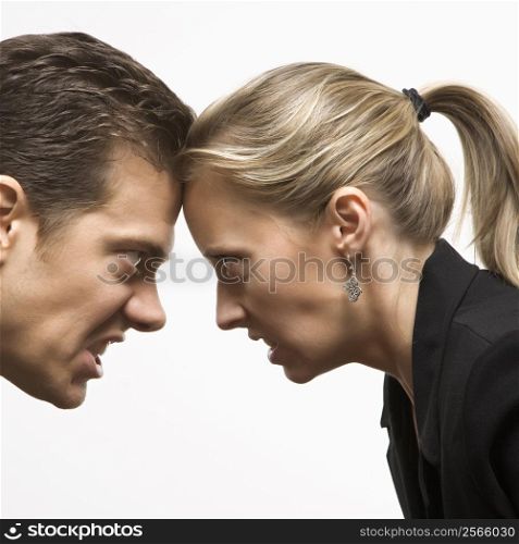 Caucasian mid-adult man and woman with foreheads together staring at each other with hostile expressions.