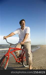 Caucasian mid-adult man posing on bicycle on beach.