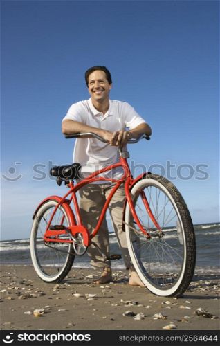Caucasian mid-adult man posing with red bicycle on beach.
