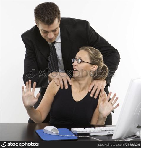 Caucasian mid-adult man sexually harassing woman sitting at computer.