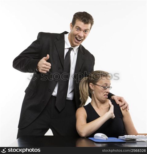 Caucasian mid-adult man sexually harassing woman sitting at computer and giving thumbs up.