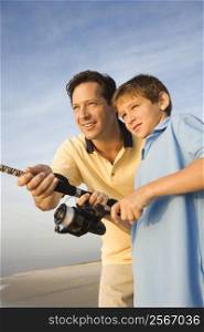 Caucasian mid-adult man shore fishing on beach with pre-teen boy