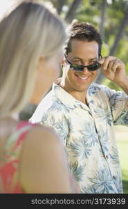 Caucasian mid adult man tilting sunglasses at woman.