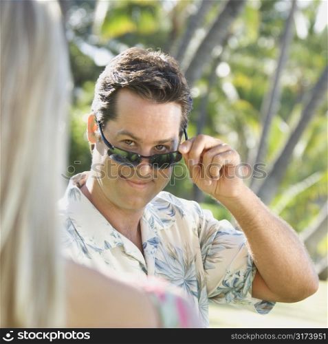 Caucasian mid adult man tilting sunglasses at woman.