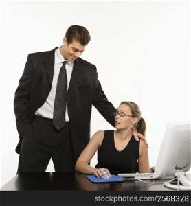 Caucasian mid-adult man touching shoulder of woman sitting at computer who feels uncomfortable.