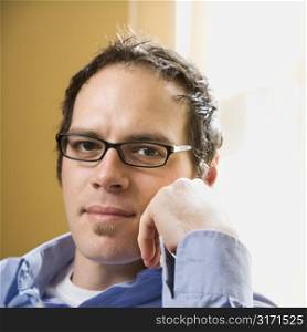 Caucasian mid adult man wearing glasses and looking at viewer with hand to face.