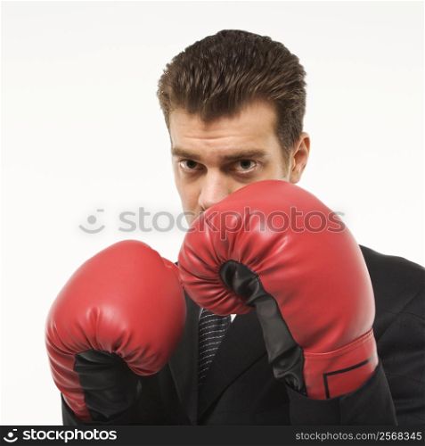 Caucasian mid-adult man wearing suit and holding boxing gloves close to his face.