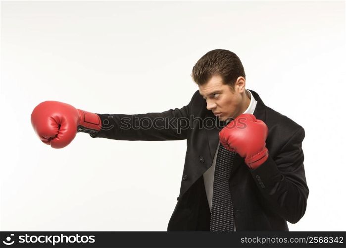 Caucasian mid-adult man wearing suit and punching with boxing gloves.