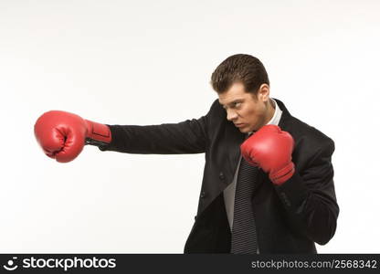 Caucasian mid-adult man wearing suit and punching with boxing gloves.